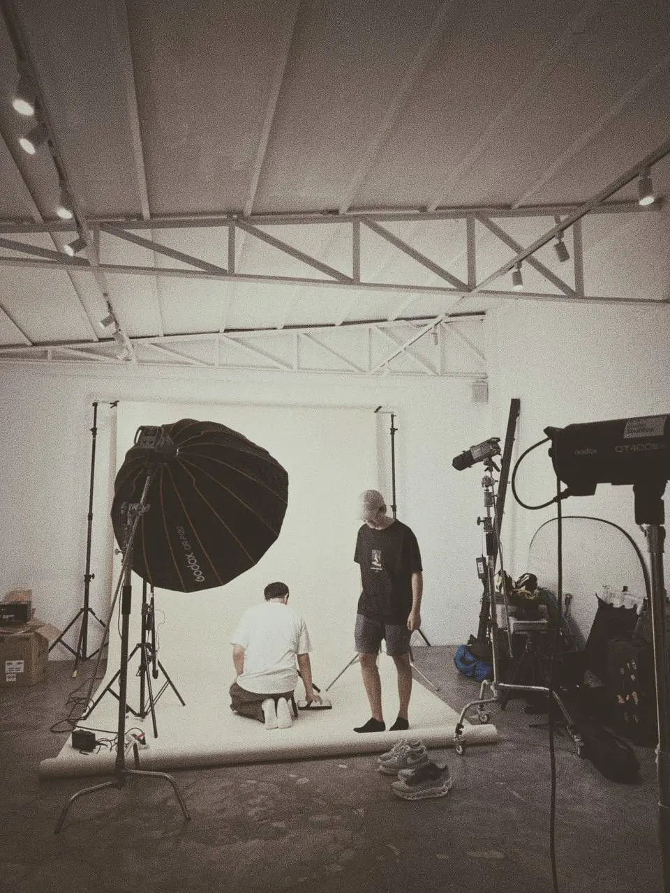 Behind the scenes at a studio shoot: two crew members set up a product on a paper backdrop surrounded by lights.